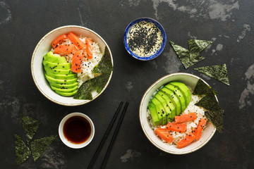 Bowl with Hawaiian salmon poke , rice, avocado and nori on a dark stone background. Top view, copy space. Sushi bowl