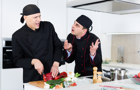 Men cooks  in black uniform discussion and having quarrel on kitchen