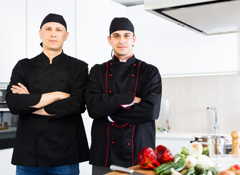 Portrait of men cook who are standing on their work place in the kitchen
