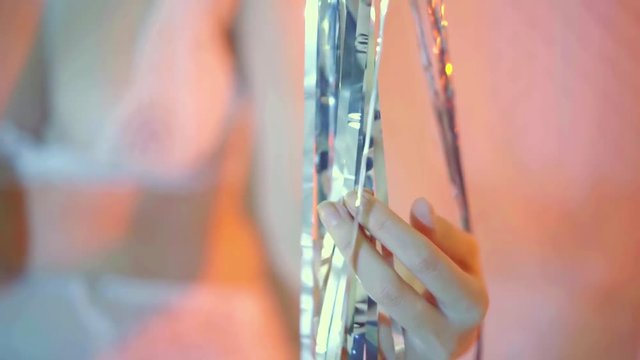 Close-up shot of a girl in a sexy white lingerie touching hanging christmas decorations in the room.