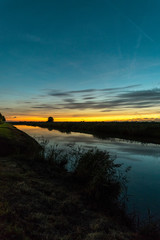 Twilight sky over a river in Holland. Beautiful colors in the sky and reflections in the calm water. Photographed between the cities of Gouda and Leiden in The Netherlands.