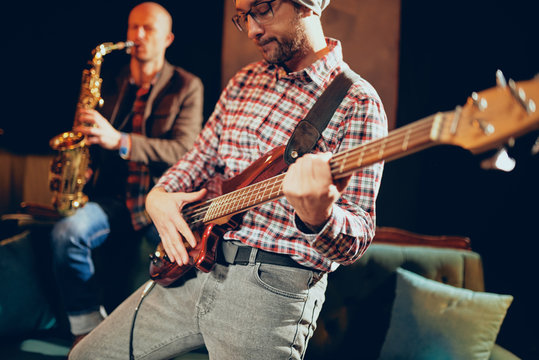 Two Caucasian great musicians playing bass guitar and saxophone while standing in home studio.