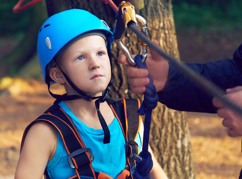 Cute little boy in blue shirt and helmet having fun at the adventure park, holding ropes and prepering to climb wooden stairs. Hobby, active lifestyle concept. - Powered by Adobe