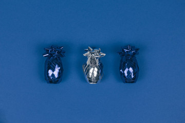 Christmas ornament of two blue and one silver shiny decorations shaped like pineapples lined on dark blue background.