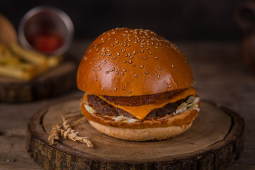 Hamburger with french fries, ketchup, mustard and fresh vegetables on a cutting wooden board.