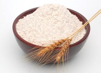 Whole flour in wooden bowl with wheat ears isolated on white background