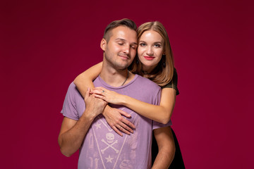 Young nice couple posing in the studio, express emotions and gestures, smiling, on a burgundy background