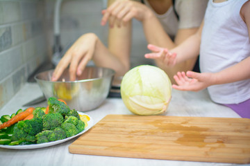 happy young woman with little daughter cooking with vegetables at home kitchen. Healthy eating concept. Vegan food
