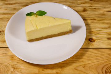 Piece of tasty sweet New York cheesecake in a white plate on wooden table