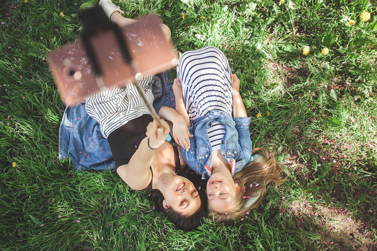 Young beautiful mother  and her little daughter making selfie at mobile phone. Mum and her baby girl outdoors having fun in the park. Girls making picture at cell phone and smiling