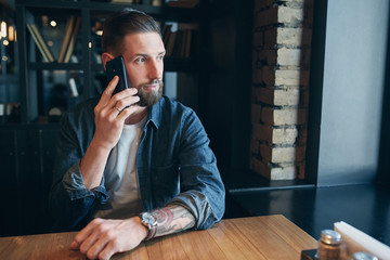 Confident young man talking on the mobile phone and smiling while sitting in cafe