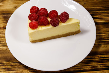 Piece of tasty New York cheesecake with raspberries in a white plate on wooden table