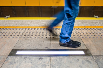 one pedestrian in blue jeans walks along tactile paving for visu