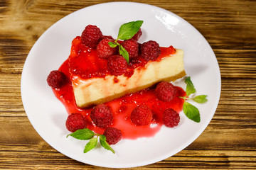 Piece of tasty New York cheesecake with raspberries and raspberry jam in a white plate on wooden table