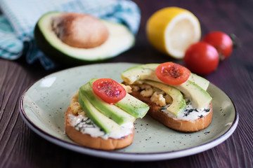 Toasts with avocado pieces, cherry tomatoes, scrambled eggs and soft cream cheese.