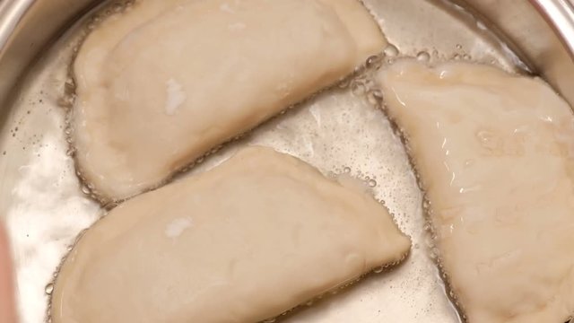 Close-up. The girl fries pasties. A female cook puts raw chebureks in a frying pan with hot oil. Cheburek fried pie with meat.