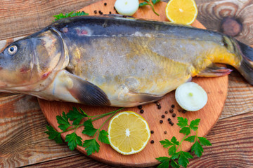 Raw carp fish with lemon, onion, pepper and parsley on cutting board on rustic wooden table