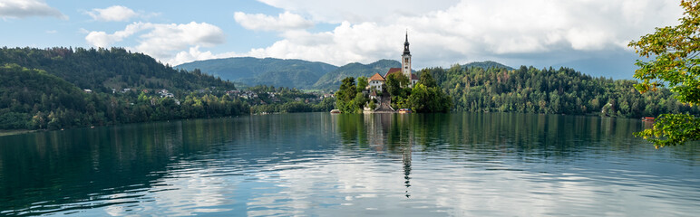 Fototapeta na wymiar Very large panoramic view on The Church of Mary the Queen, aka the Pilgrimage Church of the Assumption of Mary, located on an island in Lake Bled