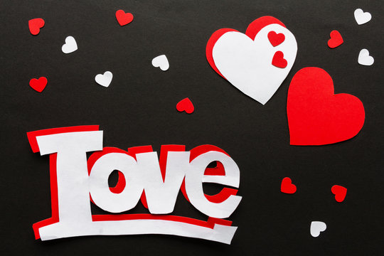 Valentines day. Paper hearts red and white on a black background. Holiday background with word love