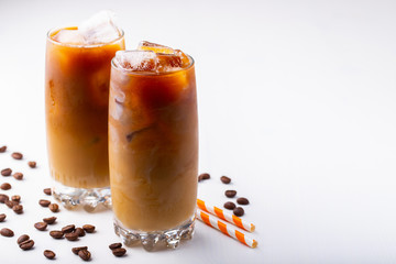 Ice coffee in a tall glass with cream poured over and coffee beans. Cold summer drink on white background with copy space