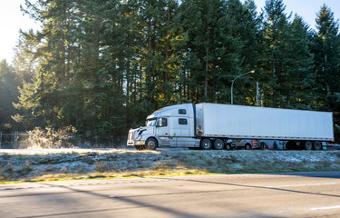 Big rig white long haul semi truck with dry van semi trailer standing on winter parking lot with...