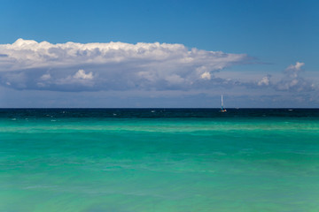 Background of turquoise sea, sky and clouds. Small sailboat at the horizon