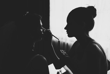 Makeup artist doing makeup for the bride.  Morning of wedding day. Black and white photo against...