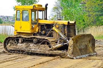 Fototapeta na wymiar Yellow crawler tractor clears the construction site for recreation on the lake.