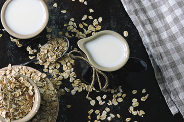 Oat milk in a milk jug on the background of oatmeal. Vegan milk. Eco food.