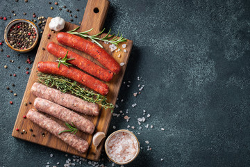 Assorted fresh sausages with thyme, rosemary, olive oil and garlic on a wooden chopping Board on a...