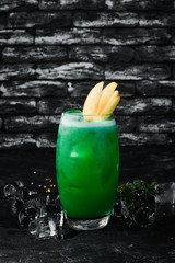 Green Alcoholic Cocktail. Tropical juice and fruit. On the black bar.