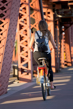 Slender girl with backpack rides bicycle on drawbridge