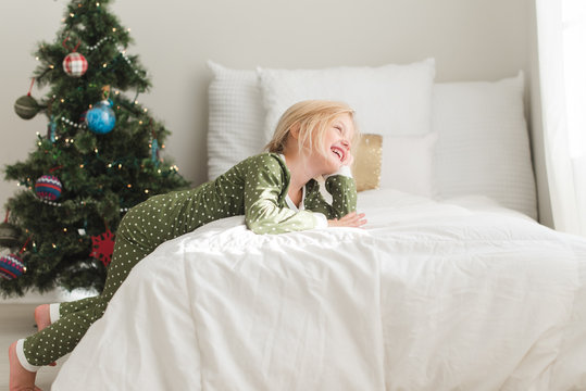 Smiling young girl leaning on a bed next to a Christmas tree