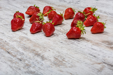 A lot of scattered fresh ripe red strawberries are lying on a light textured wooden table....