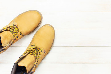 Yellow men's work boots from natural nubuck leather on wooden white background top view flat lay with copy space. Trendy casual shoes, youth style. Concept of advertising autumn winter shoes sale shop