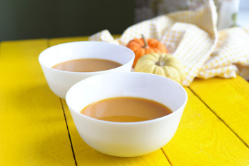 pumpkin soup and pumpkins on a yellow wooden table