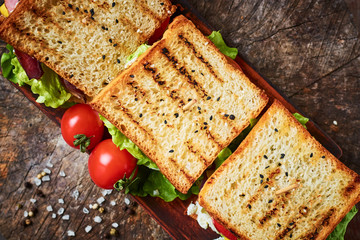 Homemade sandwich with ham, lettuce, cheese and tomato on a wooden background, top view