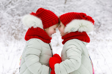 Sisters twins are touching each other with foreheads and holding a heart in hands.