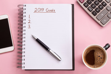 2019 goals list with notebook, cup of coffee over on pink background.