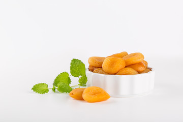 Dried Apricots in bowl with Green leaves Isolated on reflective white background