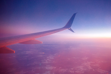 Wing of airplane with flare sun, high above clouds.