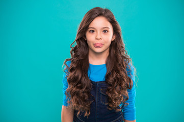 Extreme hair volume. Kid girl long healthy shiny hair. Kid happy cute face with adorable curly hairstyle stand over blue background. Teaching healthy hair care habits. Little girl grow long hair