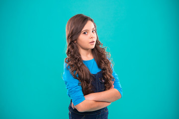 Girl curly hairstyle feels confident. Child hold hands confidently crossed chest. Child psychology and development. Confident posture. Upbringing confidence. Kid girl long hair posing confidently