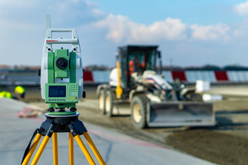 Surveyor equipment (theodolite) on construction site of the airport, building or road with construction machines in background - obrazy, fototapety, plakaty