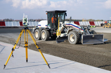 Surveyor equipment (theodolite) on construction site of the airport, building or road with construction machines in background