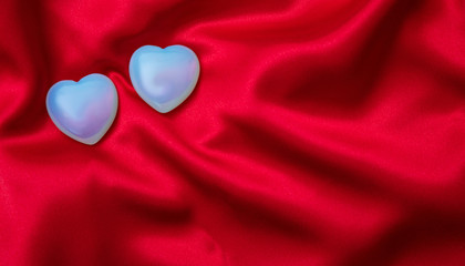Valentines day. Top view of light blue glass hearts, red silk background.