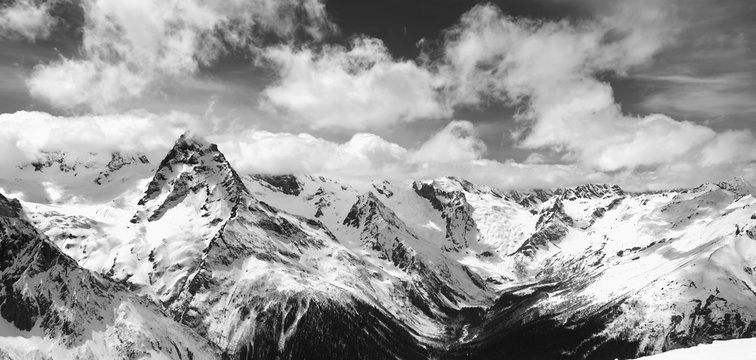 Fototapeta Black and white panorama of snowy winter mountain in sunlight clouds