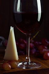 spanish wine cup with bunch of grape and pieces of cheese on dark wood stage