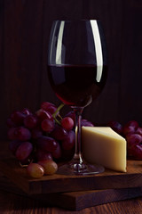 spanish wine cup with bunch of grape and pieces of cheese on dark wood stage
