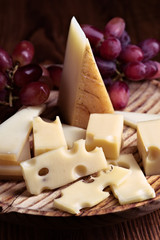 Pieces of cheese and bunches of grapes on wood illuminated with selective light